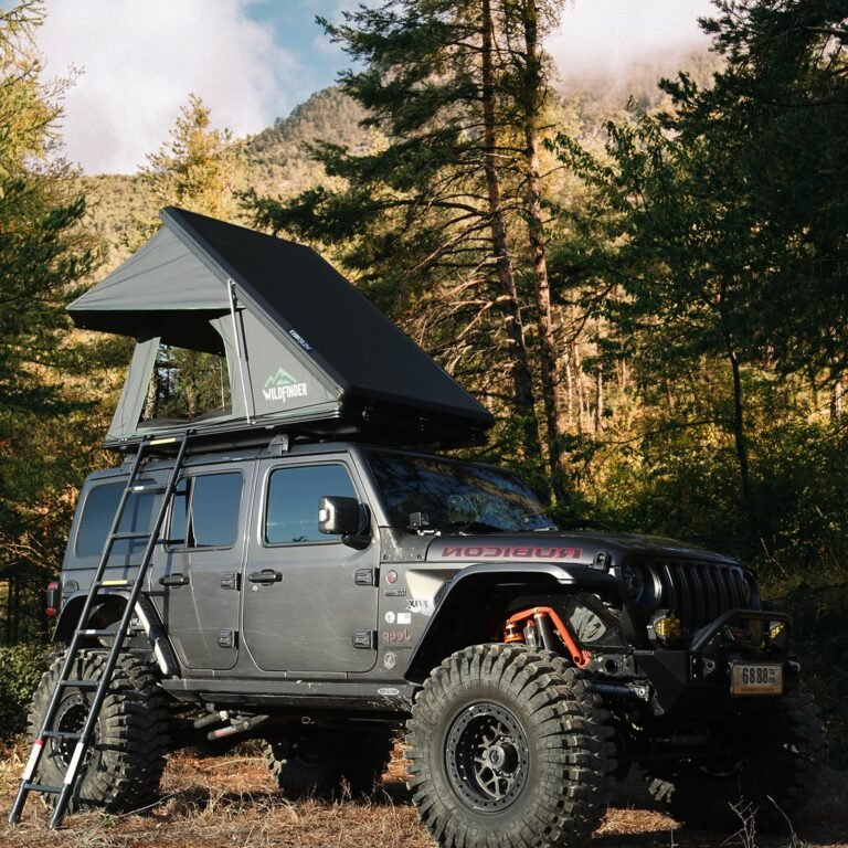 Gray Jeep Rubicon with rooftop tent and ladder in a forest setting